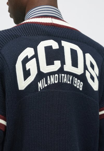Sweater de malha azul-marinho com detalhes em riscas brancas e borgonha. Apresenta texto em destaque em branco "GCDS" e "MILANO ITALY 1988" nas costas.