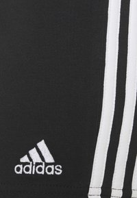 Shorts deportivos negros con un diseño de tres franjas blancas y el logotipo bordado de Adidas en la parte inferior izquierda. Fabricados con tela elástica.