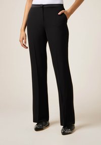 Pantaloni neri a gamba larga realizzati in tessuto morbido ed elastico. Presentano una vita piatta e tasche per la funzionalità.