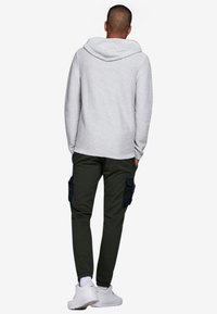 Ljusgrå, randig huvtröja med huva, i kombination med olivgrön cargobyxor med sidofickor och marinblå detaljer. Avslappnad, lös passform.