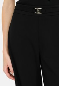 Mustad püksid, millel on sile kangas, laiad sääred ja kuldse tooni pandlaaktsent vöökohal, et saavutada peen ja elegantne välimus.
