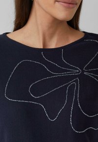 Pull marin avec un design texturé et des lignes de perles argentées formant un motif abstrait, ajusté autour de l'encolure.
