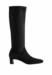 Botte noire montante en suède doux, avec un bout pointu, un petit talon bloc et une tige sans couture avec des détails de couture minimaux.