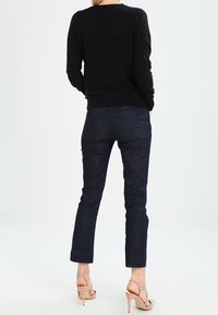 Schwarzer gestrickterPullover mit rundem Halsausschnitt, kombiniert mit dunkelblauen geraden Jeans. Das Outfit wird durch hellfarbige High-Heels Sandalen ergänzt.