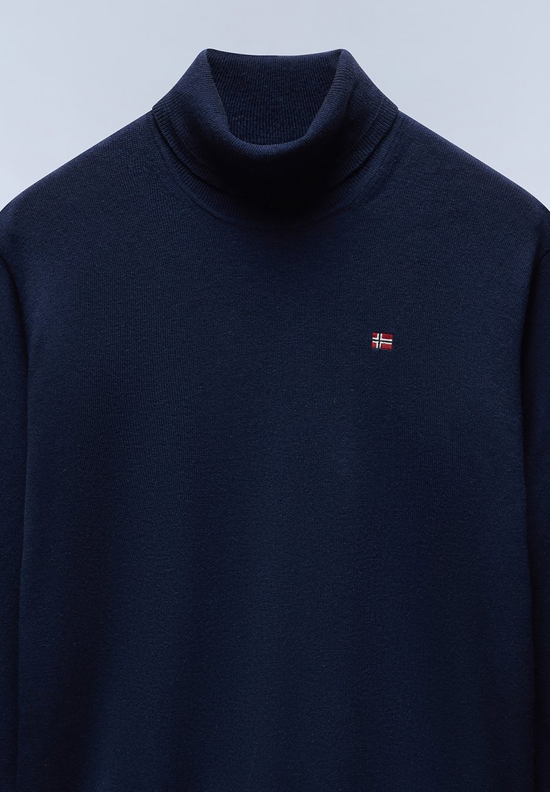 Maglione a collo alto blu navy realizzato in materiale lavorato a maglia, con un piccolo dettaglio ricamato a forma di bandiera sul petto. Texture liscia e design aderente.