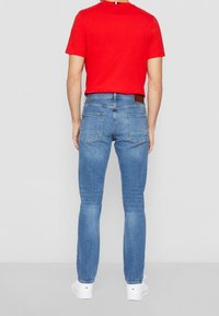 Helle blaue Skinny-Jeans mit fünf Taschen, dezenten Nähten und einem braunen Lederpatch am Bund, kombiniert mit einem roten T-Shirt mit Rundhalsausschnitt.