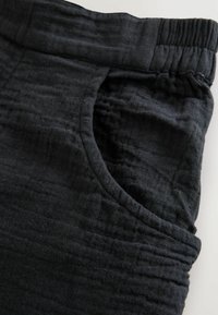 Tissu noir texturé avec une taille froncée et une poche latérale. Présente des lignes horizontales subtiles pour une apparence douce.