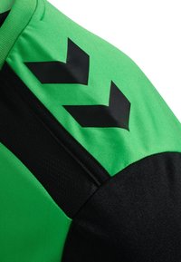 Maillot de sport vert et noir avec un tissu vert texturé et des accents noirs. Motifs en chevron noirs remarquables sur l'épaule.