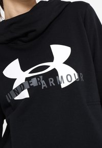 Haut à capuche noir avec un grand logo Under Armour blanc, doté d'une capuche à cordon de serrage et d'une texture de tissu douce.