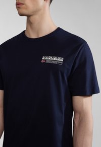 Marineblaue Baumwoll-T-Shirt mit kurzen Ärmeln, featuring ein Logo-Patch auf der linken Brust und weißen Textdetails mit "Napapijri Antarctic Research Program."