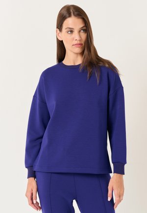 Felpa viola con scollo rotondo, spalle cadenti e polsini a costine. Realizzata in tessuto morbido con una texture liscia.