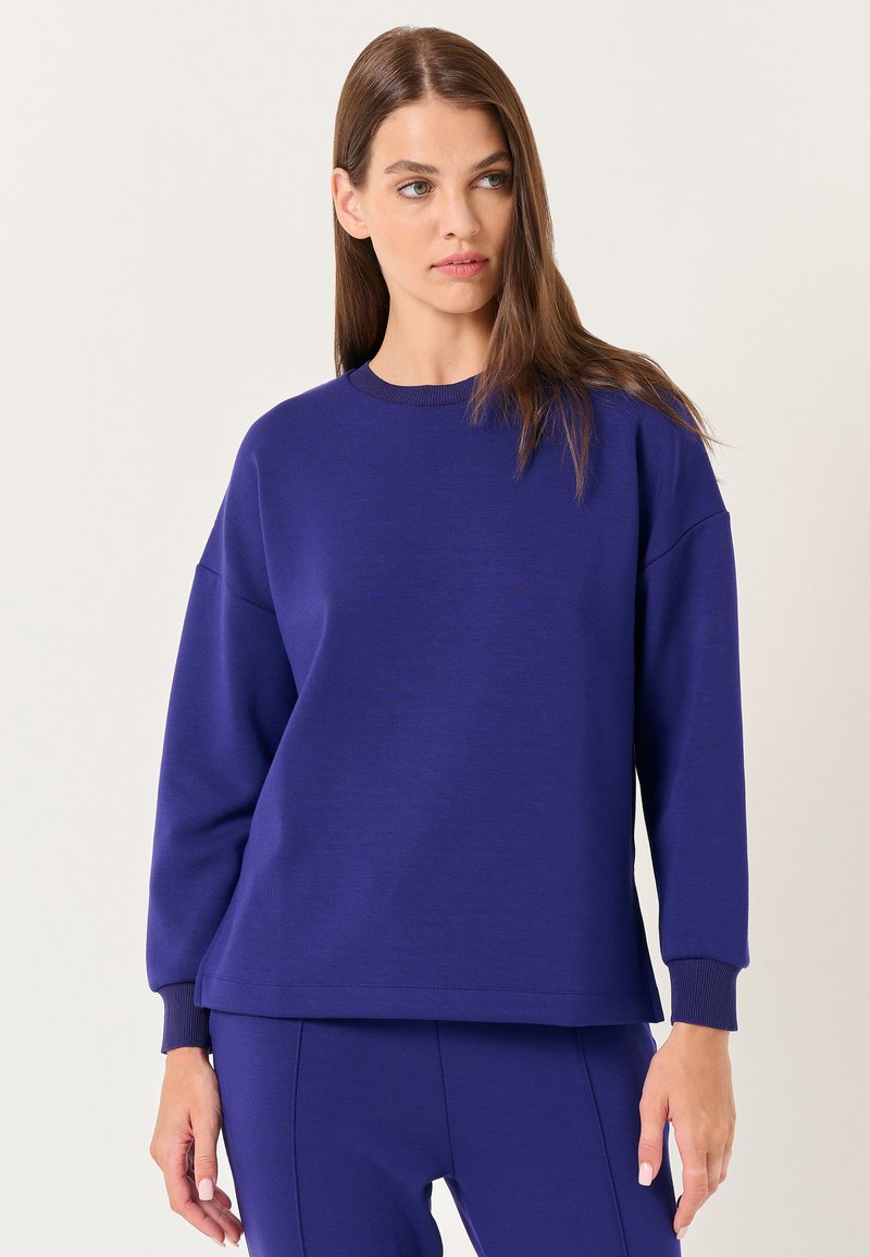 Felpa viola con scollo rotondo, spalle cadenti e polsini a costine. Realizzata in tessuto morbido con una texture liscia.