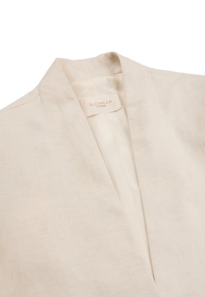 Beige linnen blazer met een diepe V-halslijn, voorzien van een zichtbare binnenlabel met de tekst "SLOWEAR MONTEVIDEO".