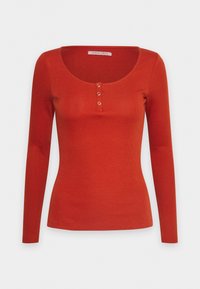 Långärmad ribbad topp i mörkröd färg, med rundad halsringning och tre dekorativa knappar fram i mitten.
