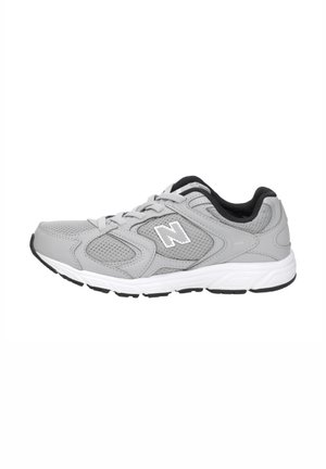 Baskets athlétiques grises et blanches avec des panneaux en maille, fermeture à lacets, semelle amortie et doublure intérieure noire, vues de profil.