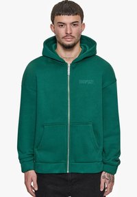 Grøn zip-hoodie lavet af blødt stof med en rummelig hætte, kengurulommer og "DROPSIZE" logo trykt på fronten.