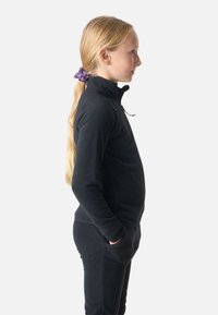 Musta fleece-paita korkealla kauluksella ja osittaisella vetoketjulla. Suuri sileä rakenne ja sovitettu muotoilu, yhdistettynä sopiviin mustiin fleece-housuihin.