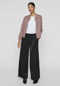 Lyserød bomberjakke med ribbede manchetter, hvid t-shirt under, og sorte vide bukser i kombination med sorte hæle. Sømløst design og strømlinet silhuet.