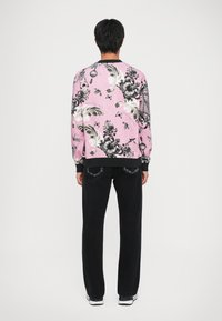 Felpa rosa con motivo floreale bianco e nero, maniche lunghe e polsini a costine. Abbinata a jeans neri in denim e sneakers bianche.