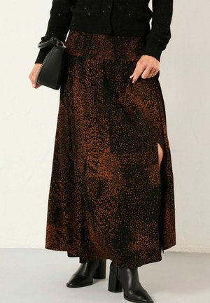 Langer schwarzer Rock mit braun gesprenkeltem Muster, ausgestattet mit einem seitlichen Schlitz. Getragen mit einem schwarzen Oberteil und schwarzen High-Heels. Kleine schwarze Handtasche.