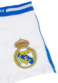 Białe slipki z niebieskim paskiem i bocznym wykończeniem, z żółtym i niebieskim herbem klubu piłkarskiego Real Madrid z koroną.
