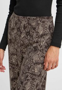 Pantalone s uzorkom zmije u smešnim i sivim tonovima, glatke teksture, sa prilagođenim krojem i srednjim strukom. Prikaz tkanine i kroja iz blizine.