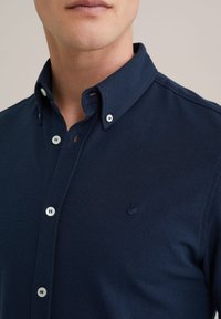 Polo de color azul marino en tejido texturizado, con cuello abotonado, botones blancos y un logo bordado en el pecho.