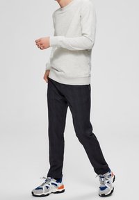 Světlě šedá mikina s kulatým výstřihem, tmavé kostkované kalhoty a vícebarevné sportovní tenisky. Neformální outfit s volným střihem a texturovanou tkaninou.