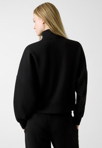 Czarna, luźna bluza z wysokim kołnierzem, długimi rękawami i swobodnym krojem. Wykonana z miękkiego, teksturowanego materiału z widocznymi szwami.