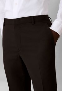 Muškarac u crnim krojenim hlačama s rukom u džepu i bijelom košuljom s gumbima stisnutom unutra.