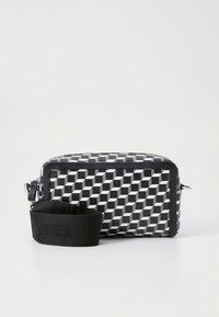 Sac à main à motif géométrique noir et blanc avec une forme rectangulaire, matériau texturé et une bandoulière noire amovible. Détails en métal argenté.
