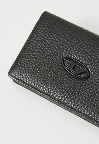 Black textured leather wallet with a smooth, raised emblem. The wallet features a compact, rectangular shape and refined stitching.
