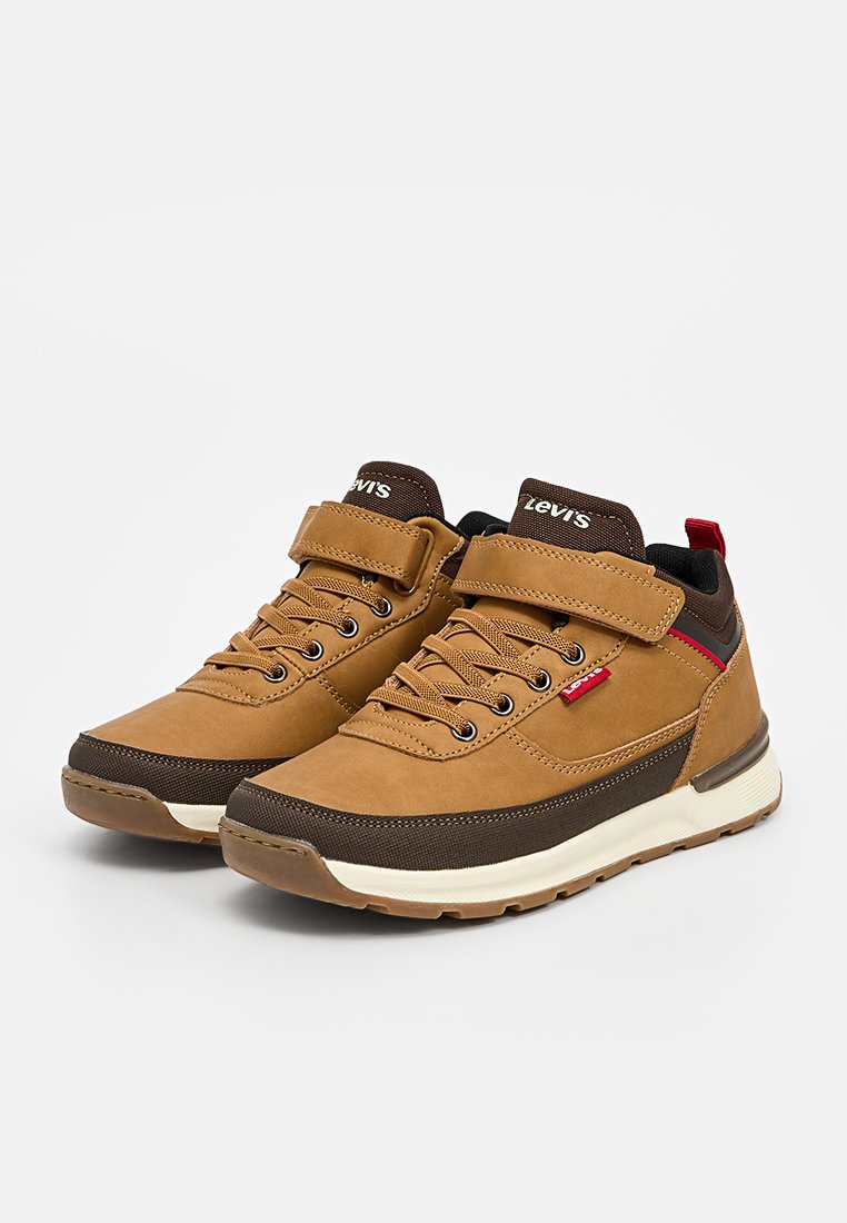 Zapatillas marrones con parte superior de tela y cuero, suelas de goma, cierre de cordones y Velcro, con acentos en rojo y negro y paneles texturizados.