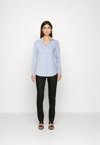 Light blue long-sleeve button-up shirt with a collar, paired with black slim-fit pants and black sandals. Smooth fabric texture.