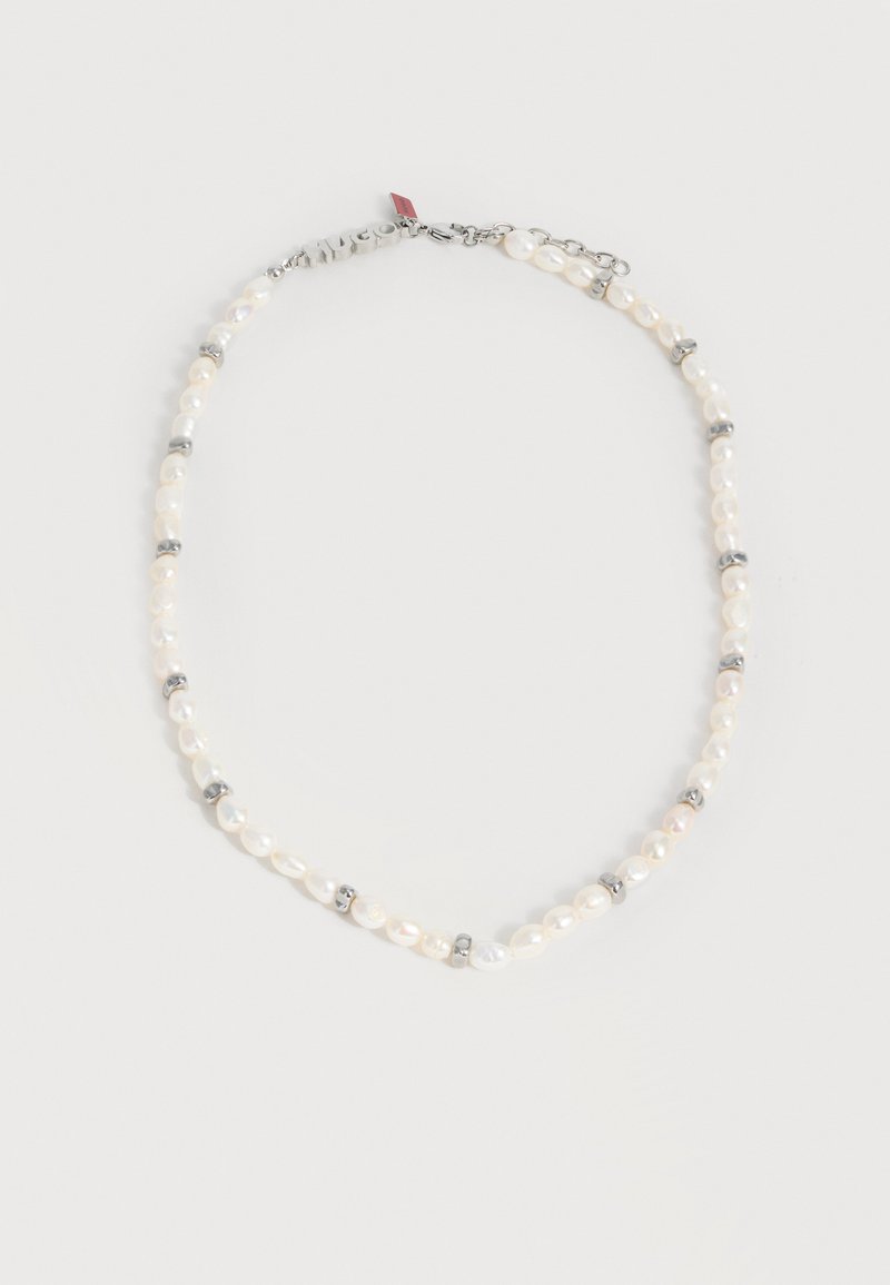 Κολιέ με λευκά ακανόνιστα μαργαριτάρια, διαχωρισμένα με μικρούς ασημένιους κρίκους, που διαθέτει ασημένια κούμπωμα και μικρή κόκκινη ετικέτα κοντά στο κούμπωμα.