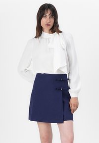 White blouse with a bow detail at the neck, paired with a navy blue mini skirt featuring two decorative bow accents. Smooth fabric texture.