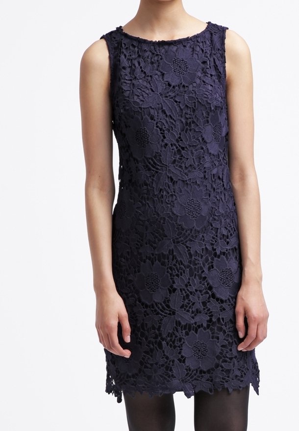 Robe sans manches en dentelle bleu marine à motif floral, longueur genou, silhouette ajustée, portée avec des collants noirs.