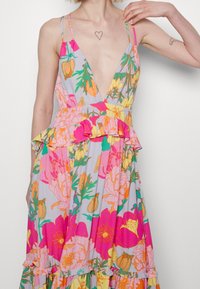 Vestido maxi floral en gris claro con vibrantes flores en rosa, naranja y amarillo, un escote en V profundo y detalles de volantes en la cintura y el dobladillo.