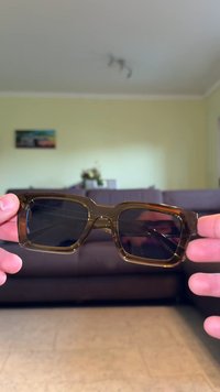 Ochelari de soare dreptunghiulari, de culoare maro, cu lentile întunecate, ramă groasă din acetat și o textură netedă. Fără modele sau accente vizibile.