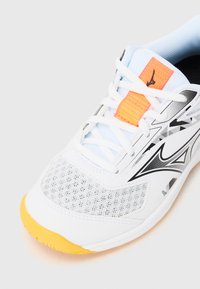 Weißer Sportschuh aus Mesh- und synthetischem Material, orangefarbenen Akzenten, schwarzem Logo, strukturiertem grauen Design und gelber Gummisohle.