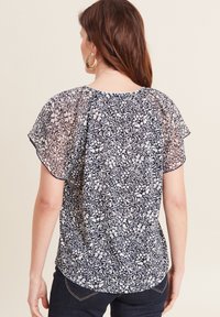 Marineblauwe blouse met een wit bloemenpatroon, korte fladdermouwen en een zachte, doorschijnende overlay. Heeft een ronde nek en elastiek in de taille.