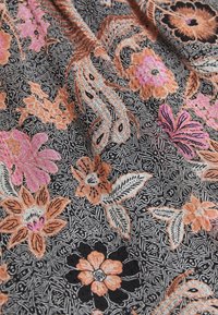 Tela con intrincados patrones geométricos en blanco y negro, superpuestos por diseños florales y de paisley en naranja, rosa y negro.