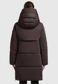 Tmavohnedý vycpan�ý parka s vysokou kapucňou. Obsahuje charakteristické logo na zadnej strane, horizontálne švy a hladkú textúru bez vzoru.