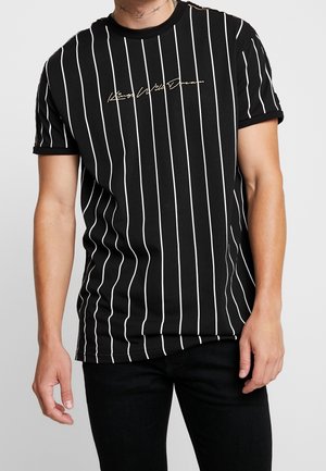 Mann trägt ein schwarzes kurzärmeliges T-Shirt mit dünnen weißen vertikalen Streifen und dem Text "King Wild Dream" über der Brust.