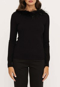 Zwarte trui met lange mouwen en een getextureerde, veerachtige halslijn. Strak ontwerp, geribbeld zoom en een gladde stofafwerking. Gekocht in combinatie met zwarte broek.