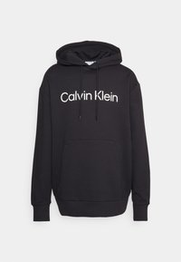 Black hoodie made of soft fabric, featuring a front pocket, drawstring hood, and the "Calvin Klein" logo in white across the chest.