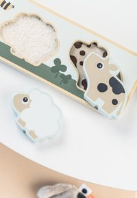 Ensemble de jouets en bois comprenant une vache et des moutons ; la vache est beige avec des taches noires, le mouton est blanc avec un bord bleu clair. Comprend des textures en feutre doux.