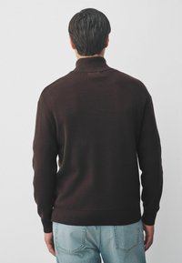 Maglione tricotato marrone scuro con colletto alto, polsini e orlo a costine, abbinato a jeans di jeans blu chiaro, mostrato di schiena.