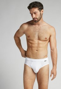 Weiße Baumwollunterhosen mit enganliegendem Schnitt, mit hohem Hüftbund und einem Vordertaschen-Design, präsentiert an einem männlichen Modell. Glatte Textur.