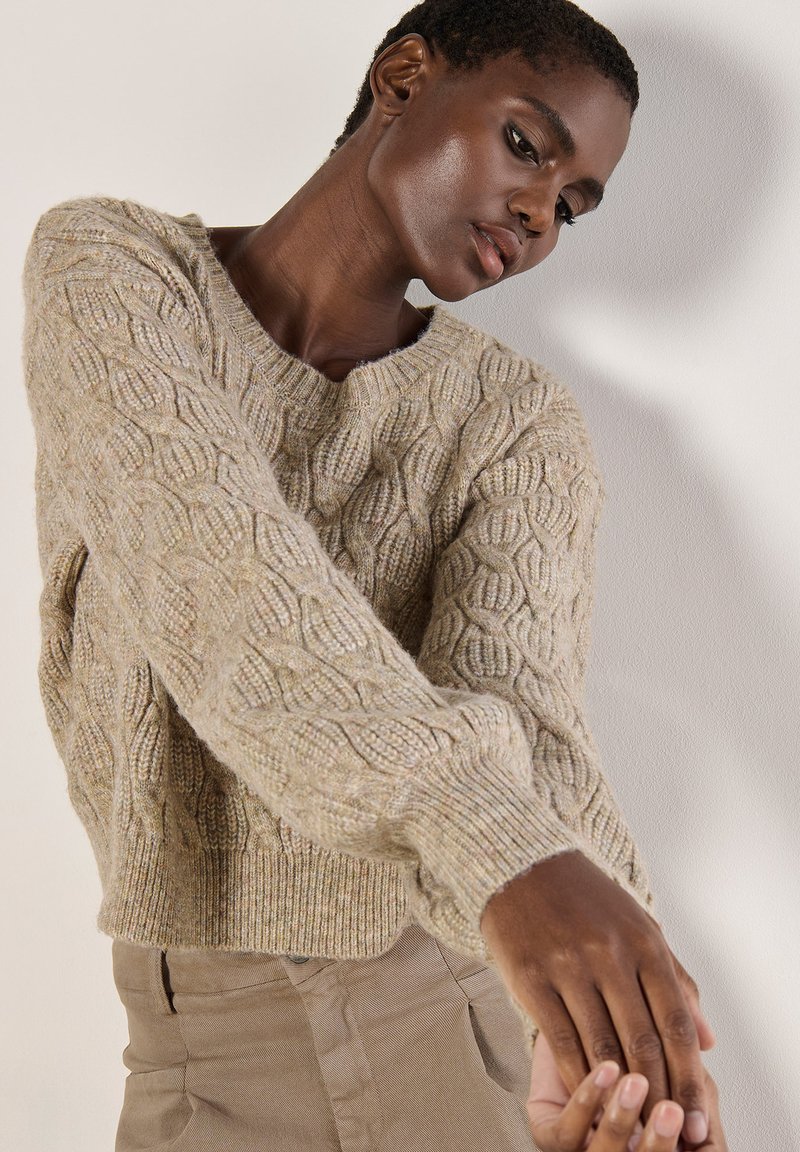 Hellebeige Kabelstrickpullover mit Rundhalsausschnitt und gerippten Bündchen, der ein strukturiertes Muster und eine verkürzte Silhouette aufweist.
